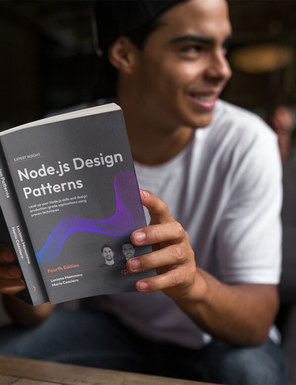 Slightly blurred young man reading a copy of Node.js Design Patterns with a smiling expression